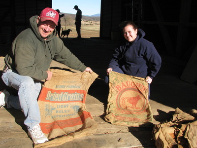 A man and a woman holding up burlap sacks that were recovered during historic barn restoration.